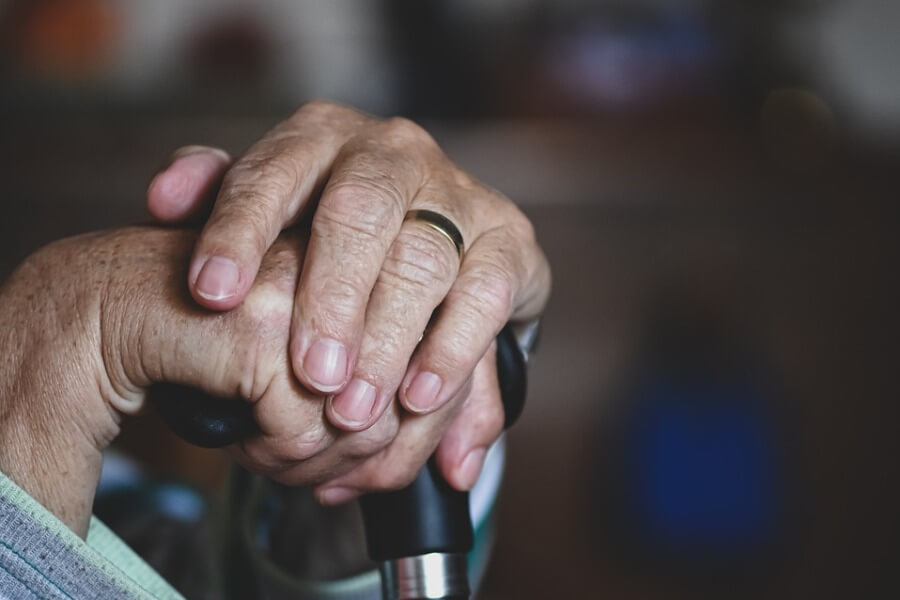 An elderly woman's hands resting on a cane.